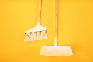 Photo of Cleaning broom and dustpan on orange background, flat lay