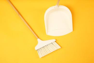 Photo of Cleaning broom and dustpan on orange background, flat lay