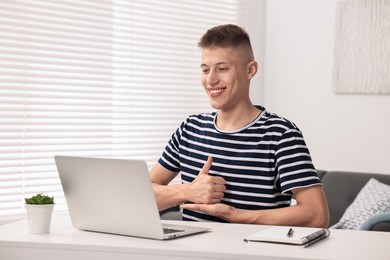 Photo of Young man using sign language during video call indoors