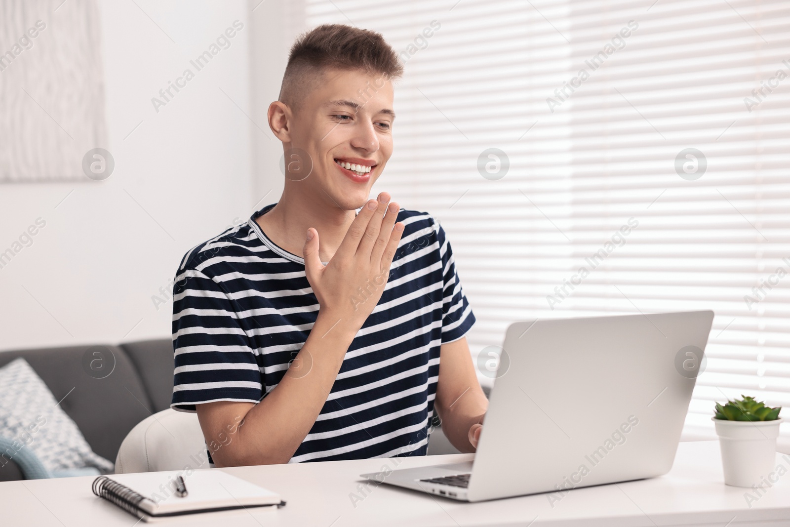 Photo of Young man using sign language during video call indoors