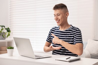 Photo of Young man using sign language during video call indoors