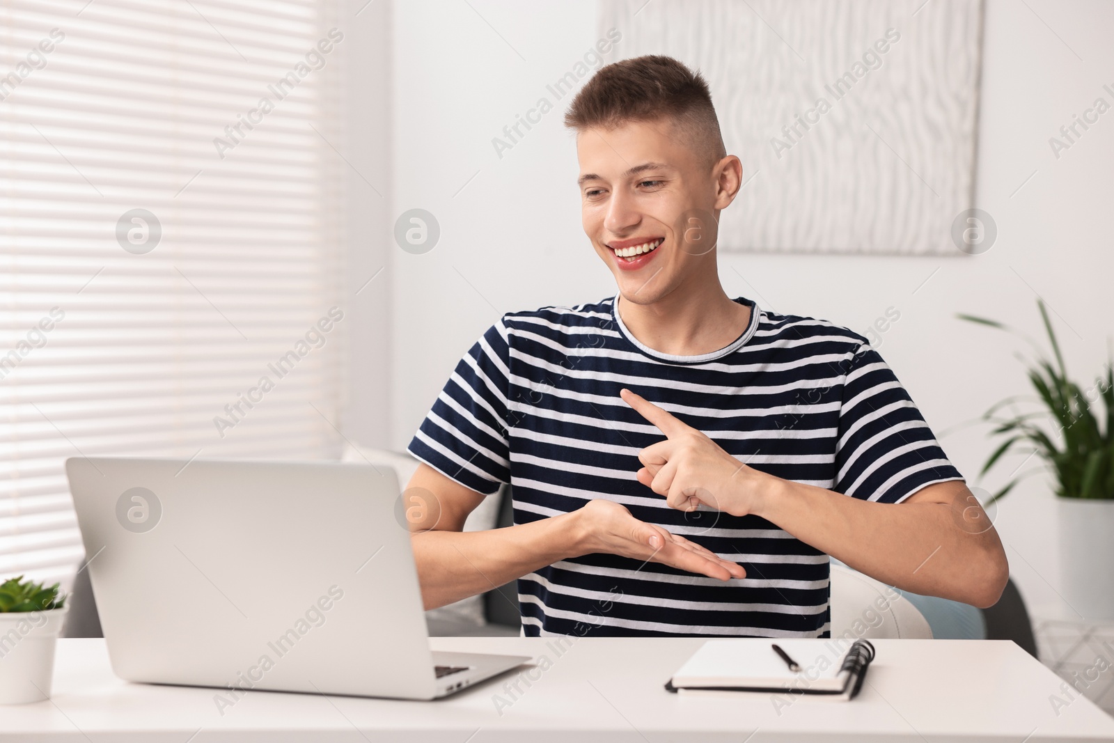 Photo of Young man using sign language during video call indoors