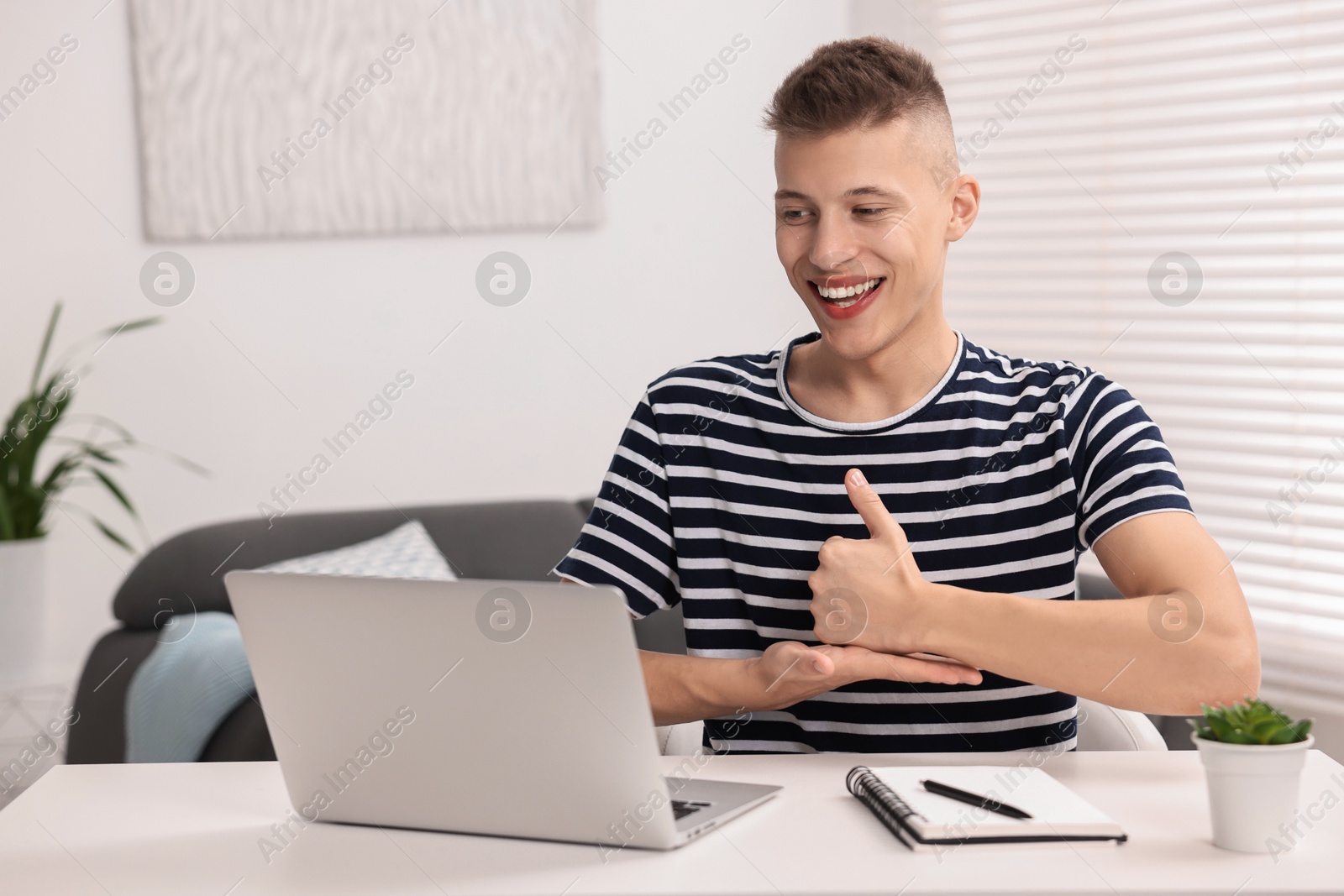 Photo of Young man using sign language during video call indoors