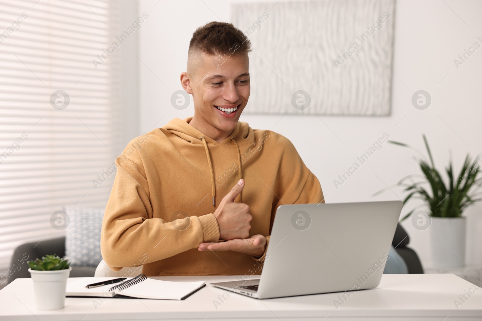 Photo of Young man using sign language during video call indoors