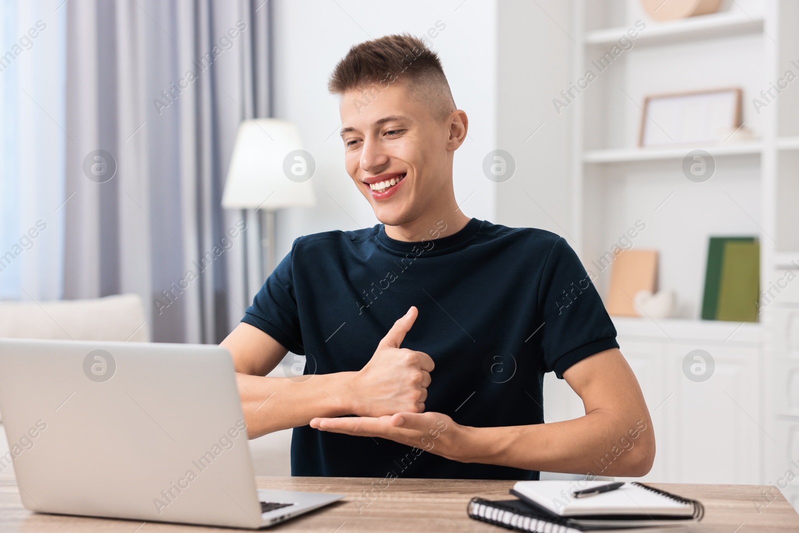 Photo of Young man using sign language during video call indoors