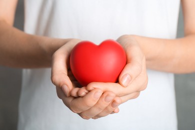 Photo of Woman holding red heart on grey background, closeup