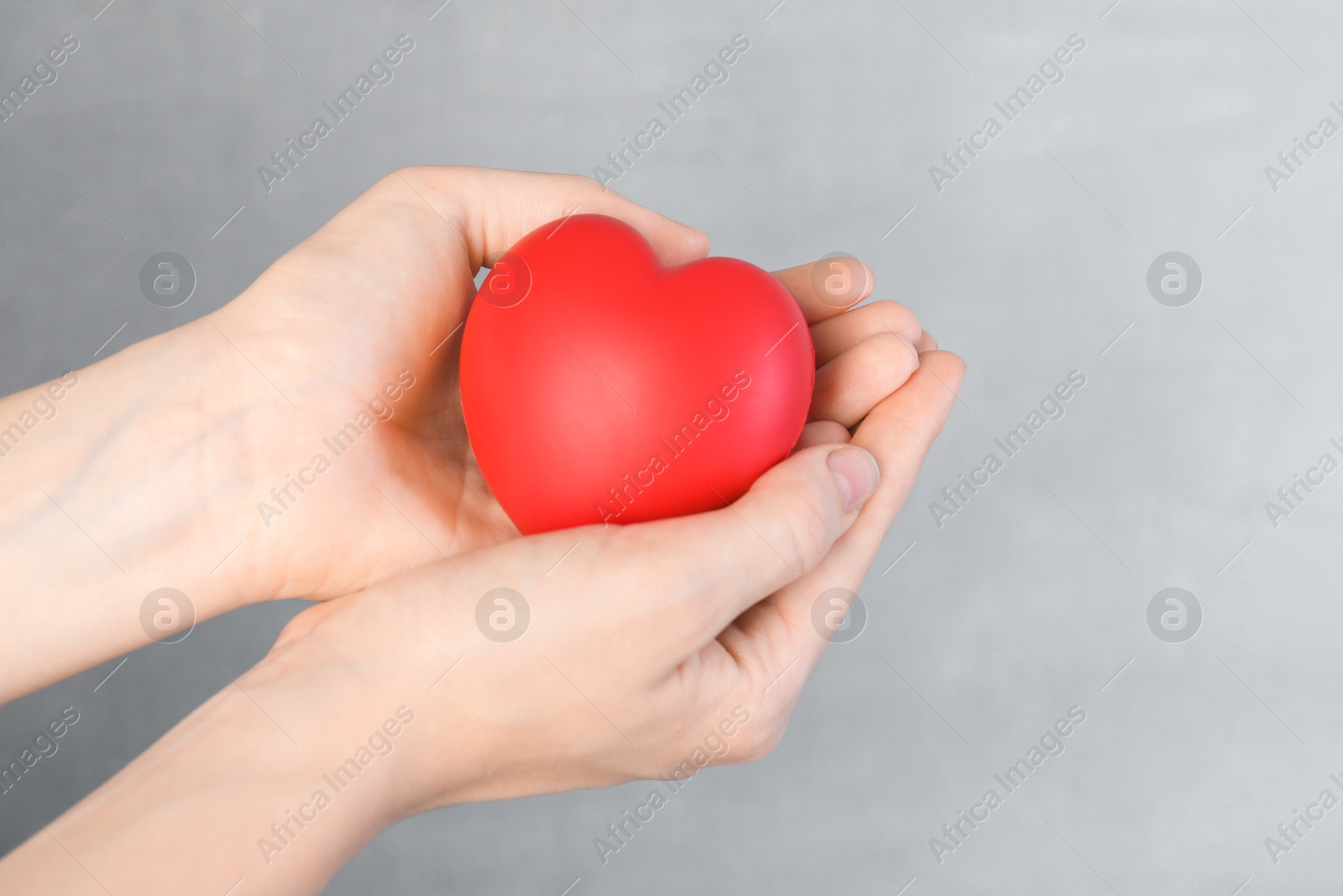 Photo of Woman holding red heart on grey background, closeup. Space for text