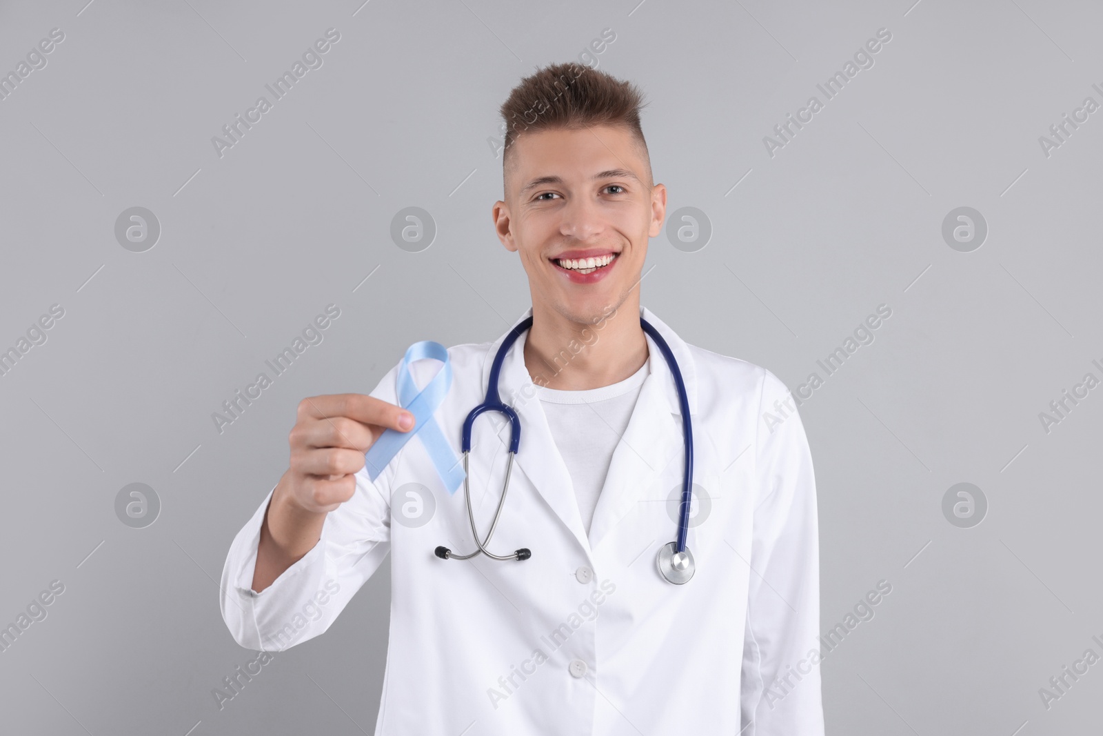 Photo of Prostate cancer awareness. Doctor holding light blue ribbon as symbol of support on grey background