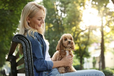 Beautiful young woman with cute dog on bench in park