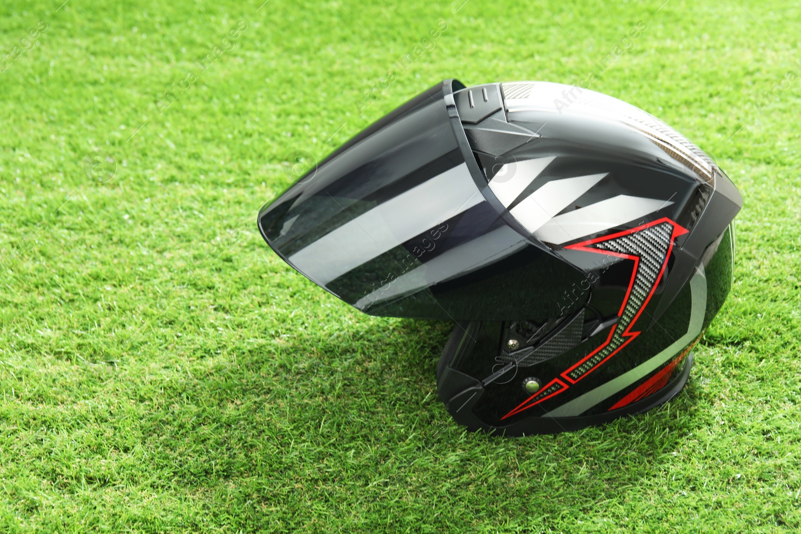 Photo of Modern motorcycle helmet with visor on green grass outdoors, space for text