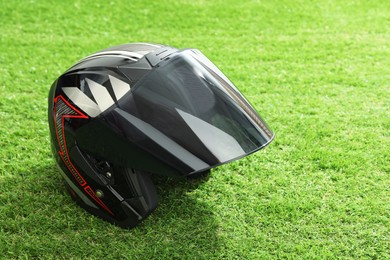 Photo of Modern motorcycle helmet with visor on green grass outdoors, space for text