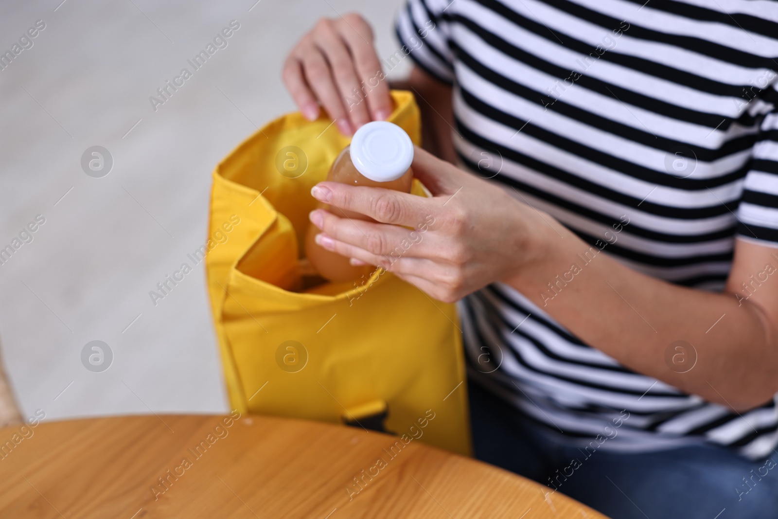 Photo of Woman putting bottle of drink into school lunch bag at wooden table indoors, closeup