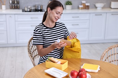 Smiling woman preparing lunch box with healthy snacks at wooden table in kitchen