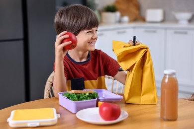 Photo of Cute boy with lunch box, healthy products and bag at wooden table in kitchen