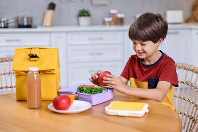 Photo of Cute boy with lunch box, healthy products and bag at wooden table in kitchen