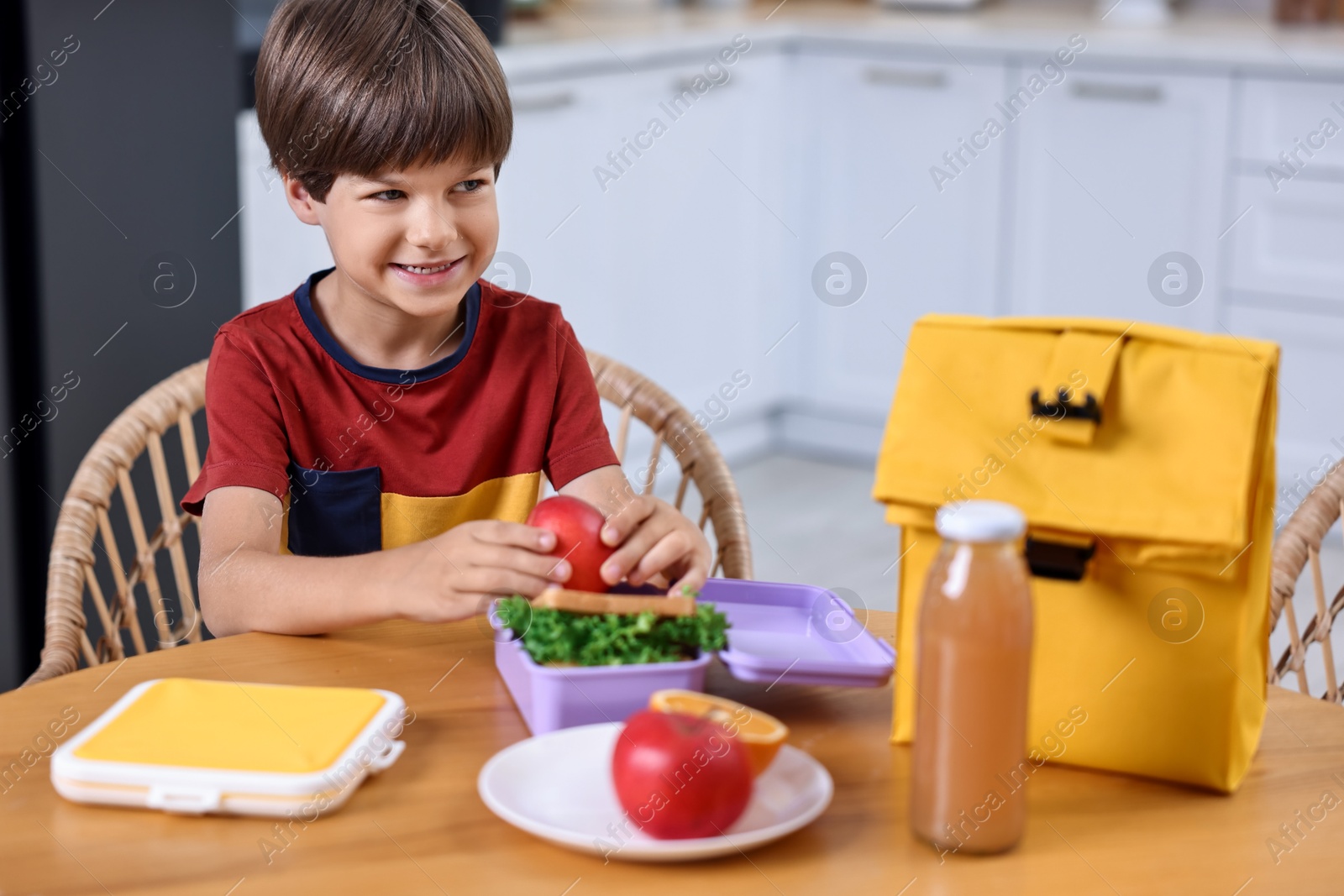 Photo of Cute boy with lunch box, healthy products and bag at wooden table in kitchen