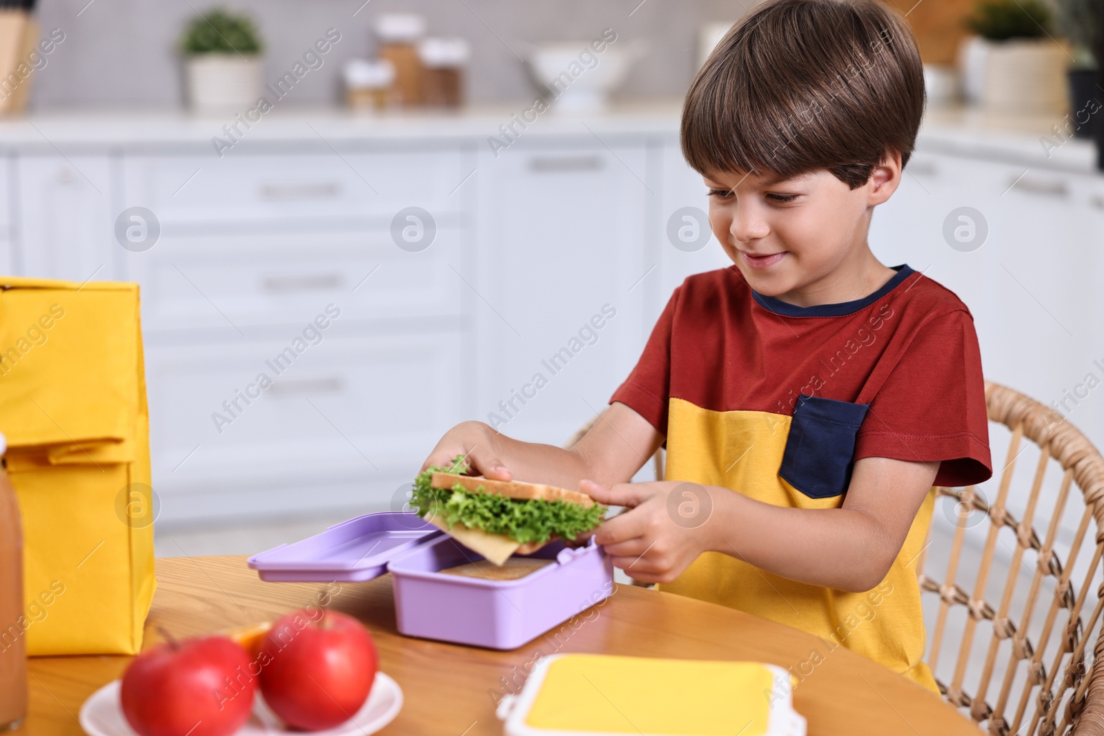 Photo of Cute boy with lunch box, healthy products and bag at wooden table in kitchen