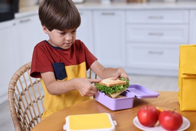 Photo of Cute boy with lunch box, healthy products and bag at wooden table in kitchen