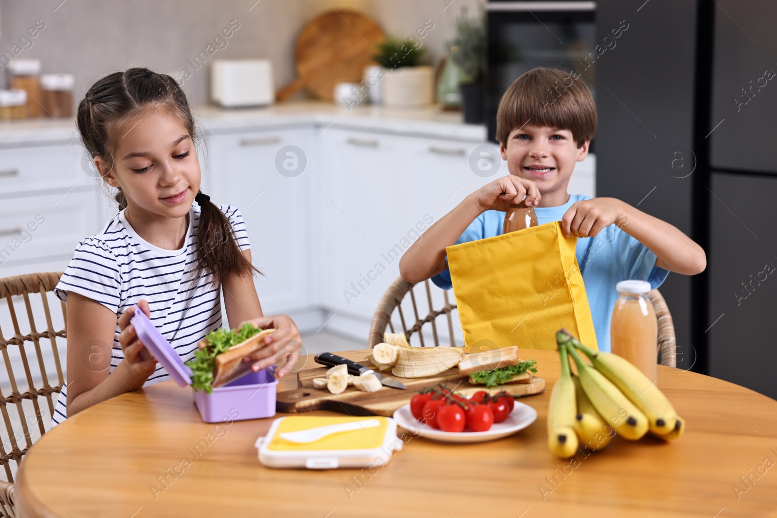 Photo of Cute children with healthy snacks preparing lunch box at wooden table in kitchen