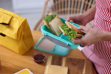 Photo of Woman packing school lunch box with healthy snacks at table in kitchen, closeup