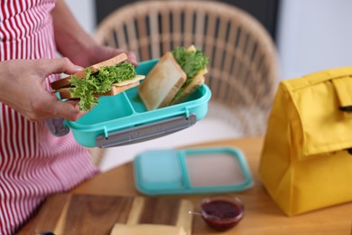 Photo of Woman packing school lunch box with healthy snacks at table in kitchen, closeup