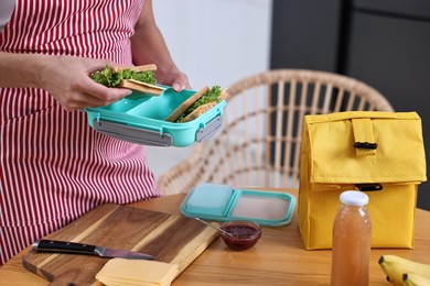 Photo of Woman packing school lunch box with healthy snacks at table in kitchen, closeup