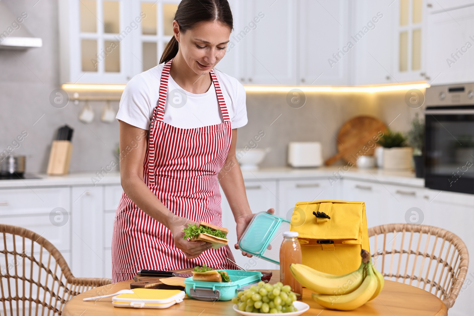 Photo of Woman packing school lunch box with healthy snacks at wooden table in kitchen