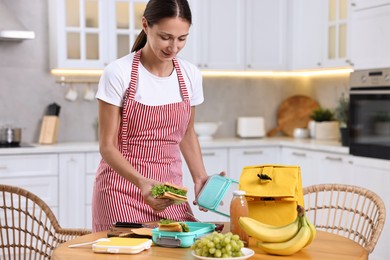 Woman packing school lunch box with healthy snacks at wooden table in kitchen