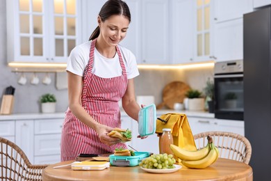 Woman packing school lunch box with healthy snacks at wooden table in kitchen