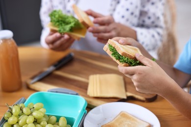 Boy and his mother preparing lunch box with healthy snacks at wooden table in kitchen, closeup