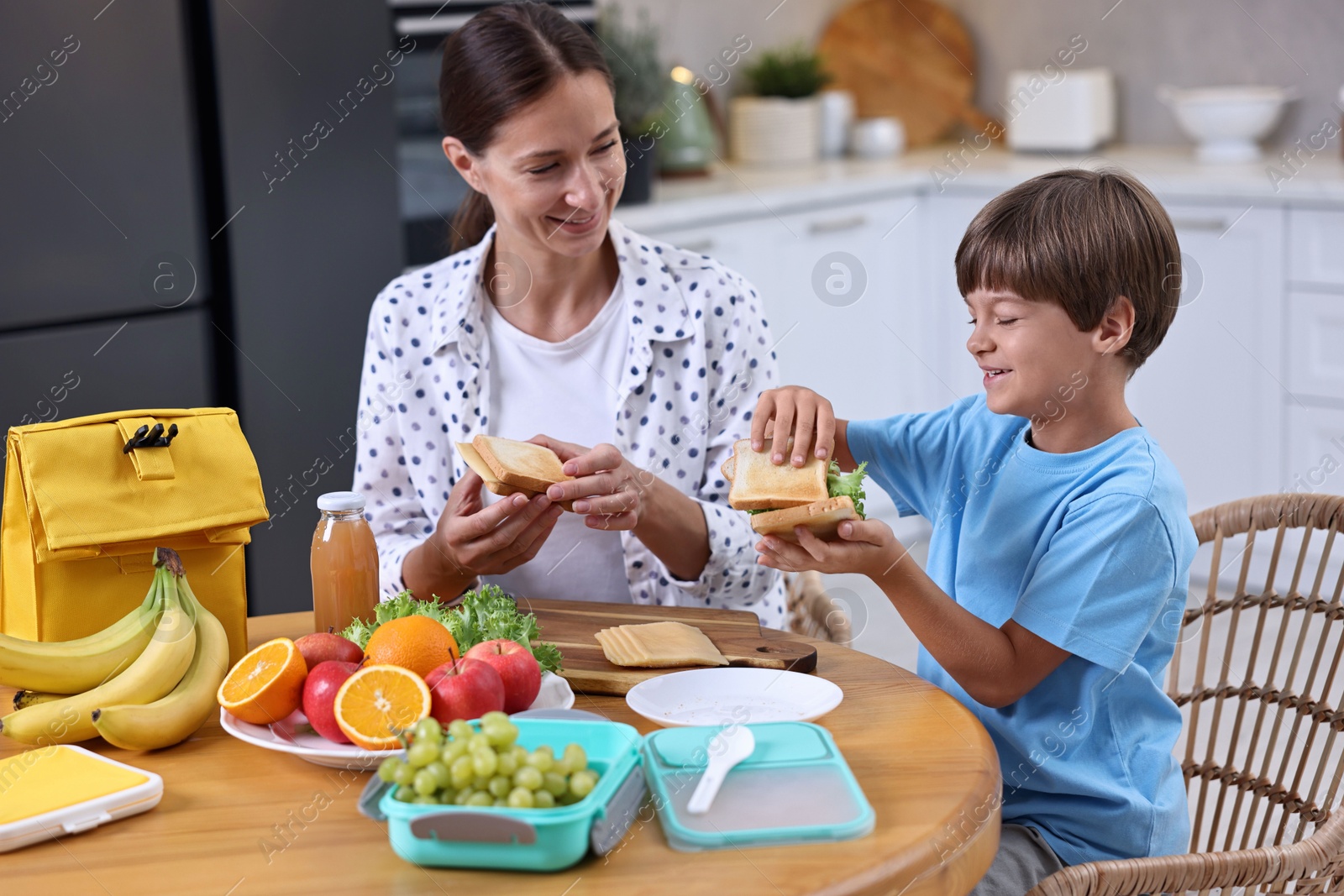 Photo of Mother and her cute son preparing lunch box with healthy food at wooden table in kitchen