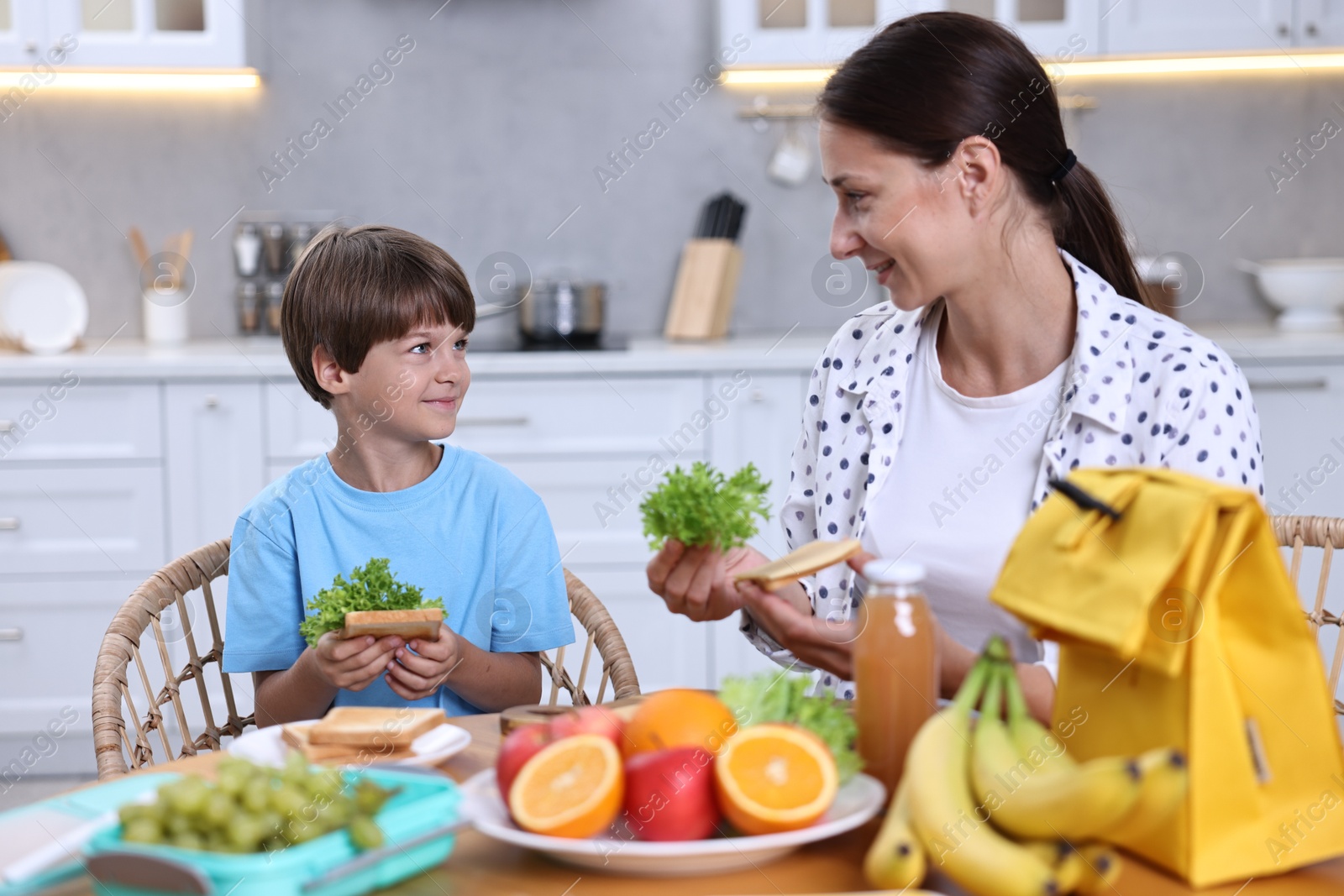 Photo of Mother and her cute son preparing lunch box with healthy food at wooden table in kitchen