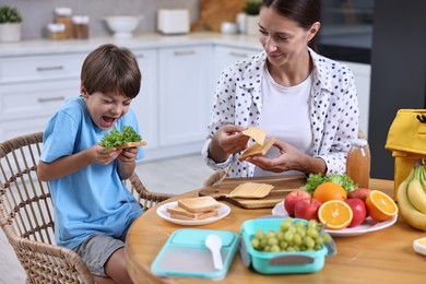 Mother and her cute son preparing lunch box with healthy food at wooden table in kitchen