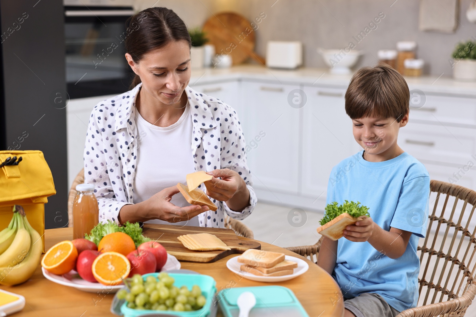 Photo of Mother and her cute son preparing lunch box with healthy food at wooden table in kitchen