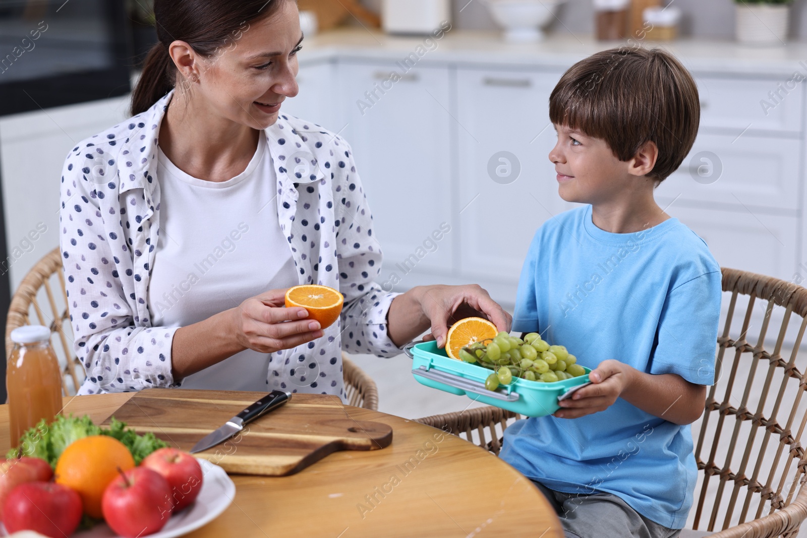 Photo of Mother and her cute son preparing lunch box with healthy food at wooden table in kitchen