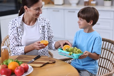 Mother and her cute son preparing lunch box with healthy food at wooden table in kitchen