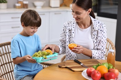 Mother and her cute son preparing lunch box with healthy food at wooden table in kitchen