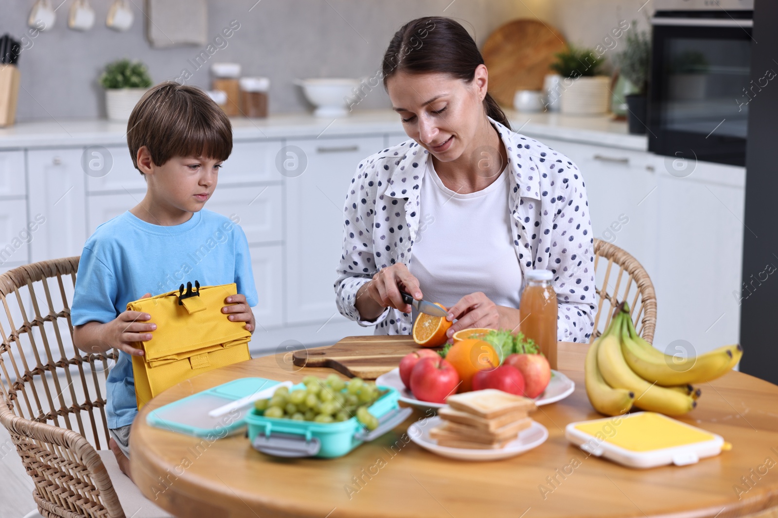 Photo of Mother and her cute son preparing lunch box with healthy food at wooden table in kitchen