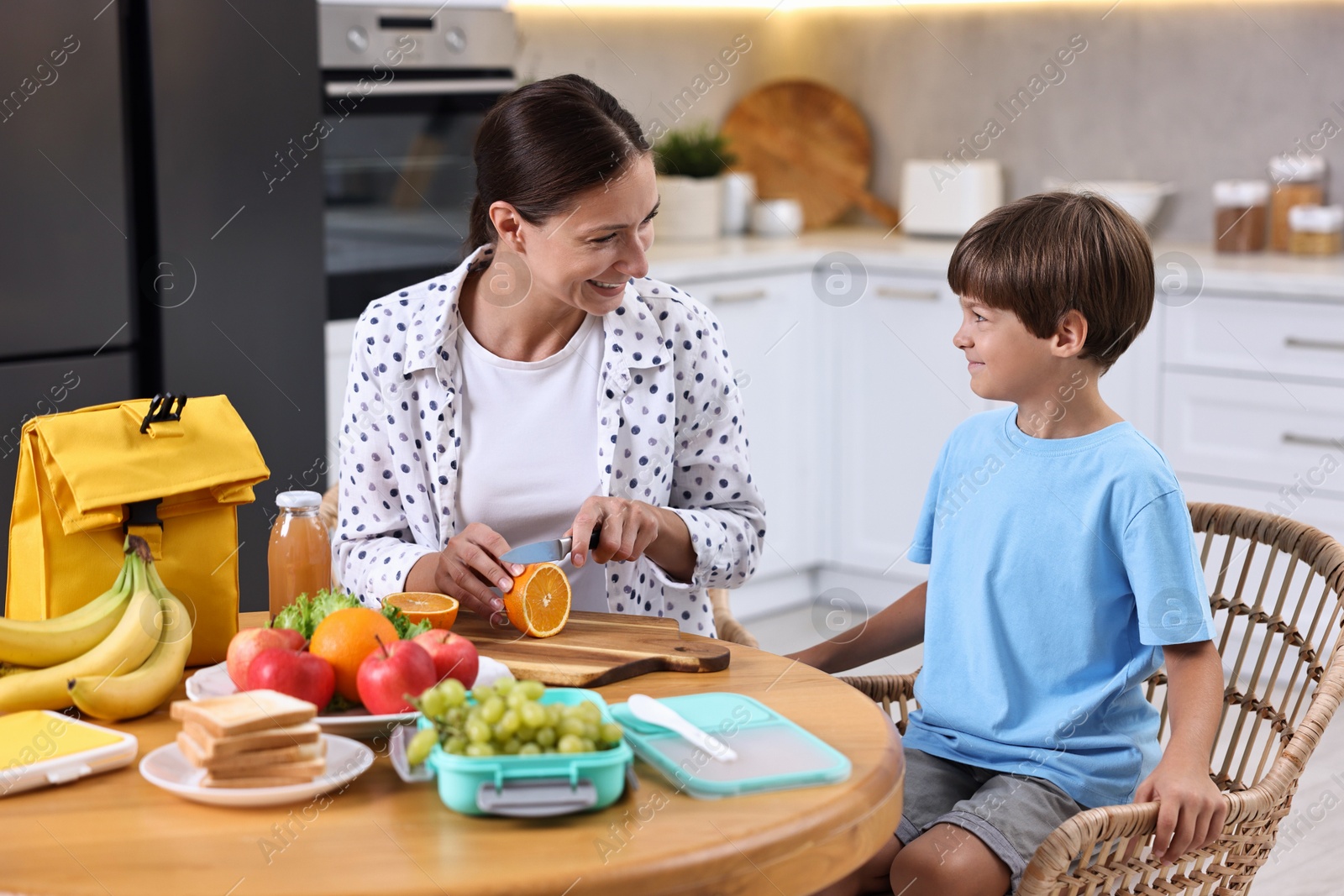 Photo of Mother and her cute son preparing lunch box with healthy food at wooden table in kitchen