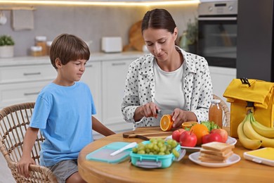 Photo of Mother and her cute son preparing lunch box with healthy food at wooden table in kitchen