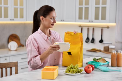 Photo of Woman with bag packing school lunch box and healthy food at white marble table in kitchen