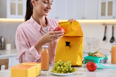 Photo of Woman packing school lunch box with healthy meal at white marble table in kitchen, closeup