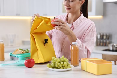 Photo of Woman with bag packing school lunch box and healthy meal at white marble table in kitchen, closeup