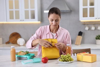 Photo of Woman with bag packing school lunch box and healthy food at white marble table in kitchen