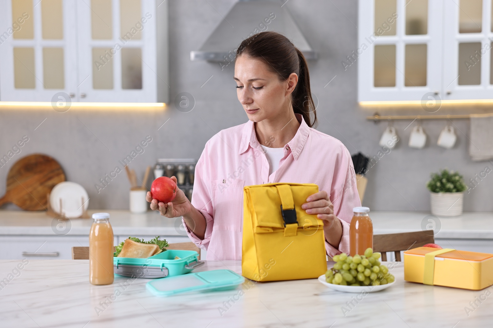 Photo of Woman with bag packing school lunch box and healthy food at white marble table in kitchen