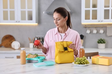 Woman with bag packing school lunch box and healthy food at white marble table in kitchen