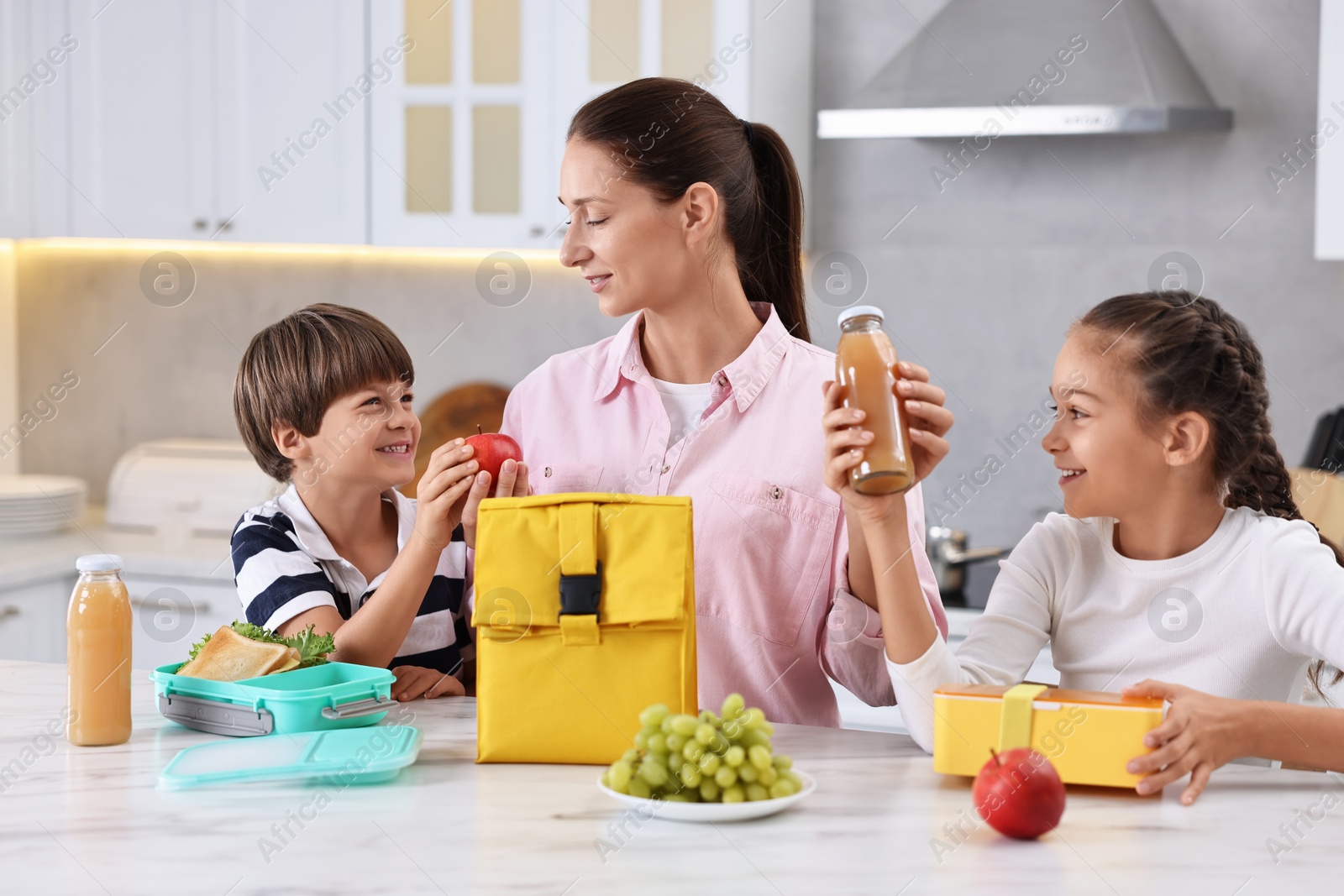 Photo of Mother and her children preparing school lunch boxes with healthy food at table in kitchen