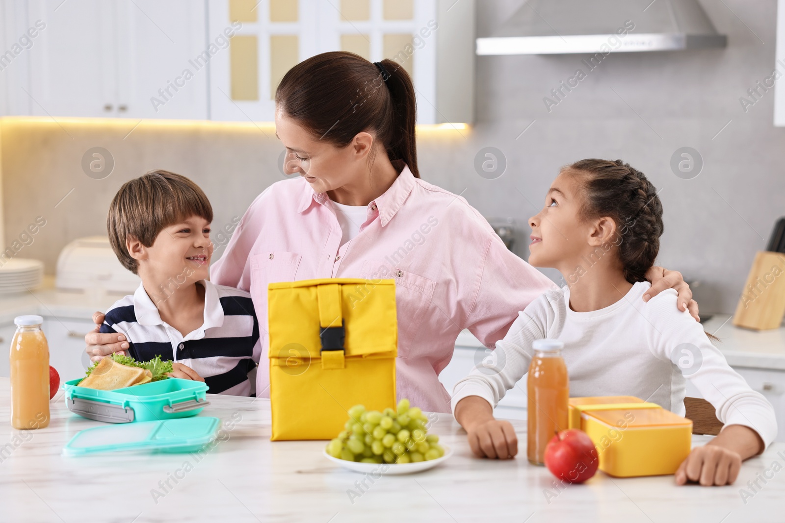 Photo of Mother and her children preparing school lunch boxes with healthy food at table in kitchen