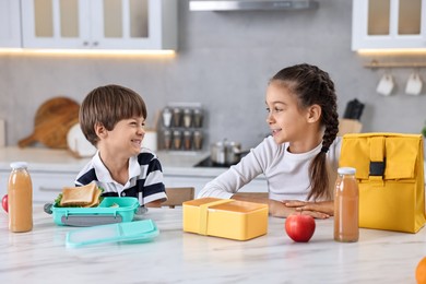 Photo of Cute children preparing school lunch boxes with healthy food at white marble table in kitchen