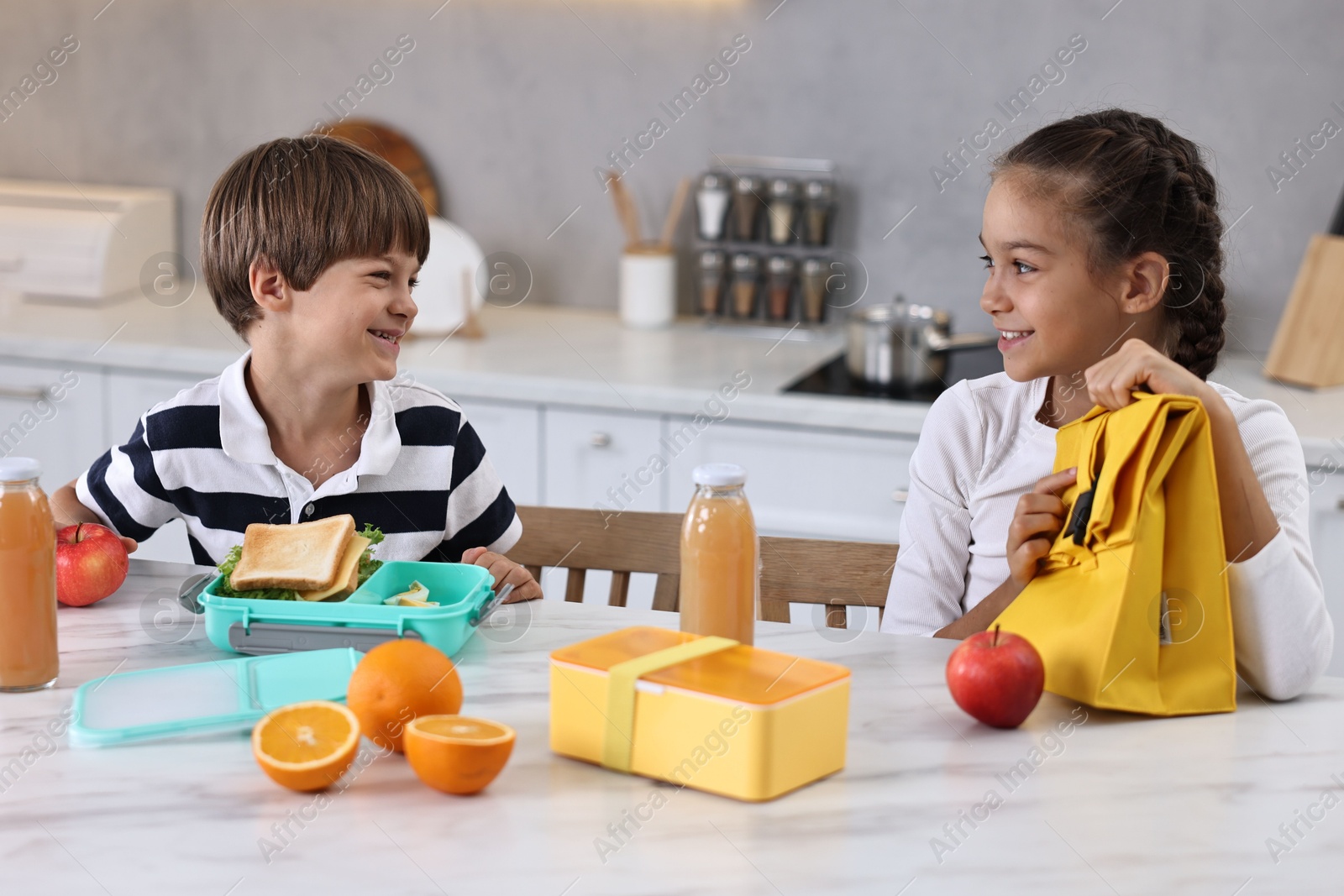 Photo of Cute children preparing school lunch boxes with healthy food at white marble table in kitchen